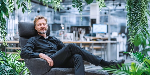 Produktionsleiter sitzt entspannt in moderner, grüner Arbeitsumgebung mit digitalen Bildschirmen – Symbolbild für KI in der Produktion.